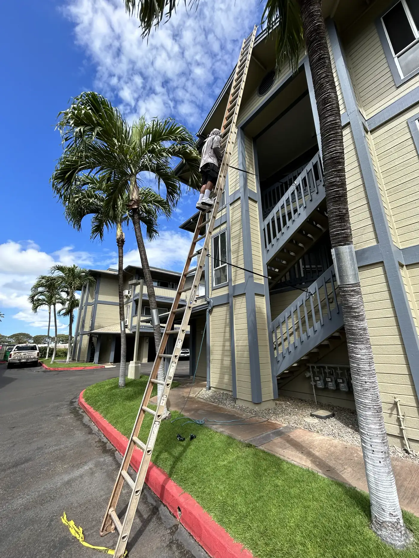A Hawaii Ladder Assist crew member climbing an extension ladder beside a two-story apartment building