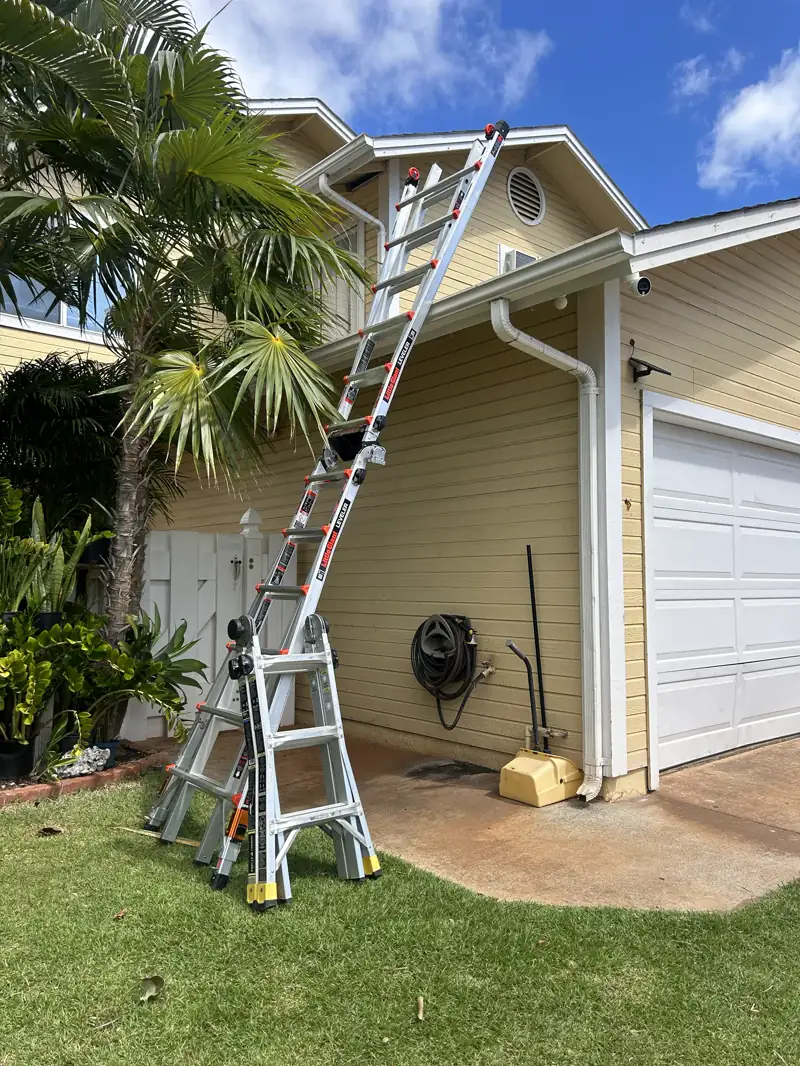 A multi-position ladder set up beside a yellow house and palm trees